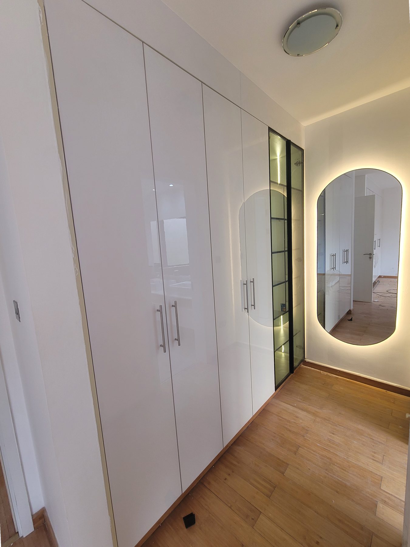 Gloss wardrobe corridor leading to a backlit oval mirror